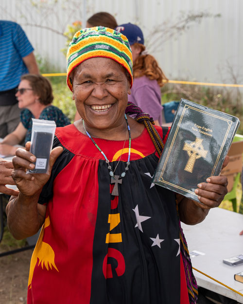 Woman smiling with printed and audio copies of Enga New Testament.